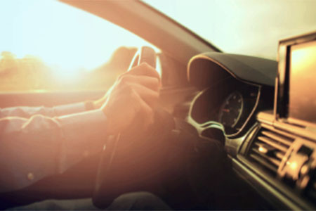Interieur eines Autos mit Händen am Lenkrad im Sonnenuntergang. Foto: Car2TERA