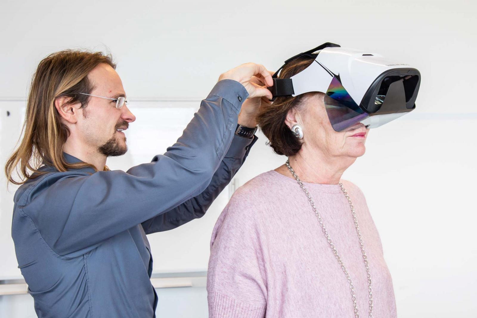 Ein Mann legt einer älteren Frau eine Virtual Reality-Brille an. Foto: FH Joanneum / Miriam Weiß