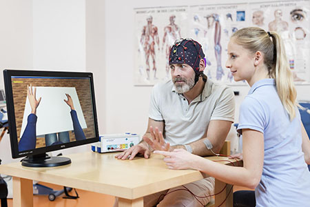 Patient mit Datenhaube und Betreuerin vor einem Bildschirm. Foto: g.tec Guger Technologies