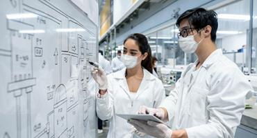 Zwei Forscher:innen vor dem Ablaufplan eines industriellen Prozesses. Foto: iStock
