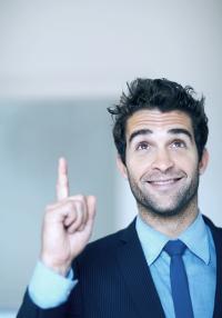 Das Foto zeigt einen fröhlichen Mann mit Anzug und Krawatte und erhobenem Zeigefinger